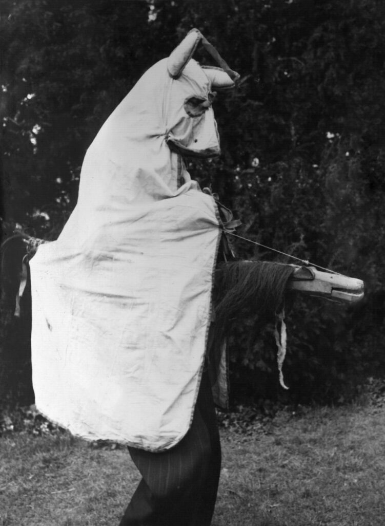 Black and white photograph of a person wearing a hobby horse costume.