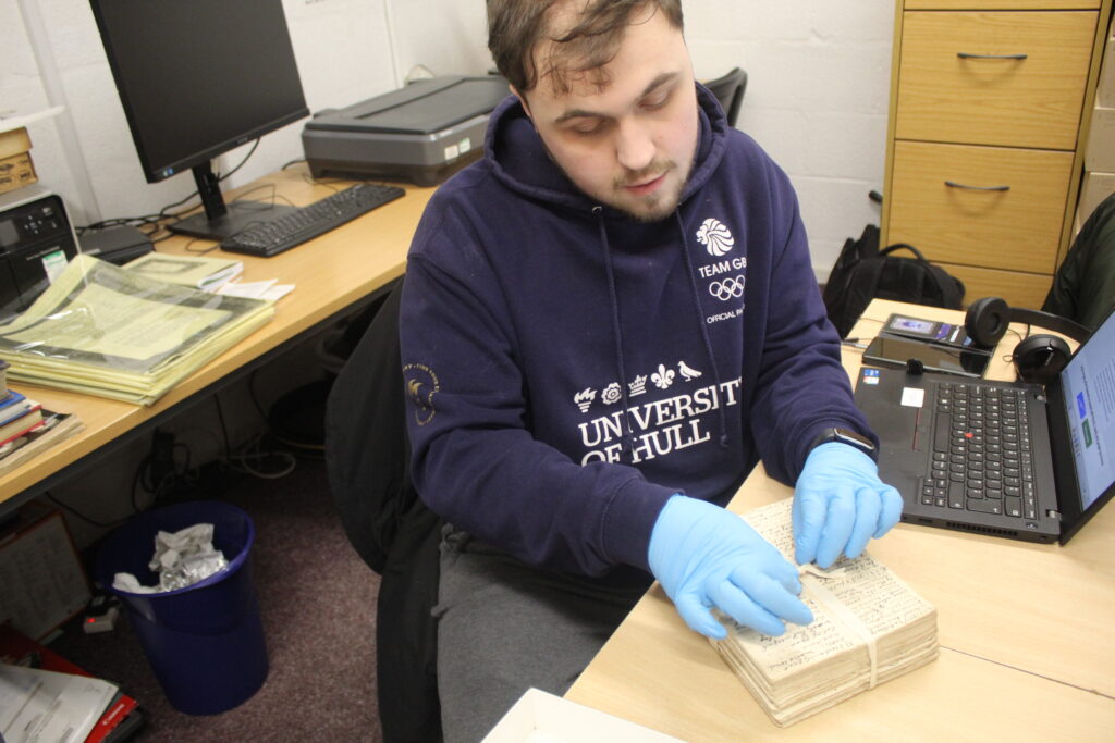 young man with brown hair, wearing blue gloves to handle a little book