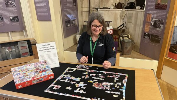 a member of the learning team with a board game with a stand of artefacts