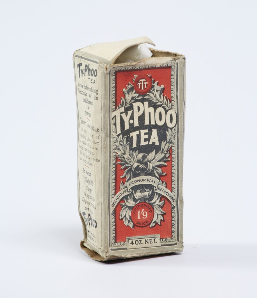 A small rectangular cardboard that once held tea bags. The front decorated with a blue and white wreath style logo on a red background.