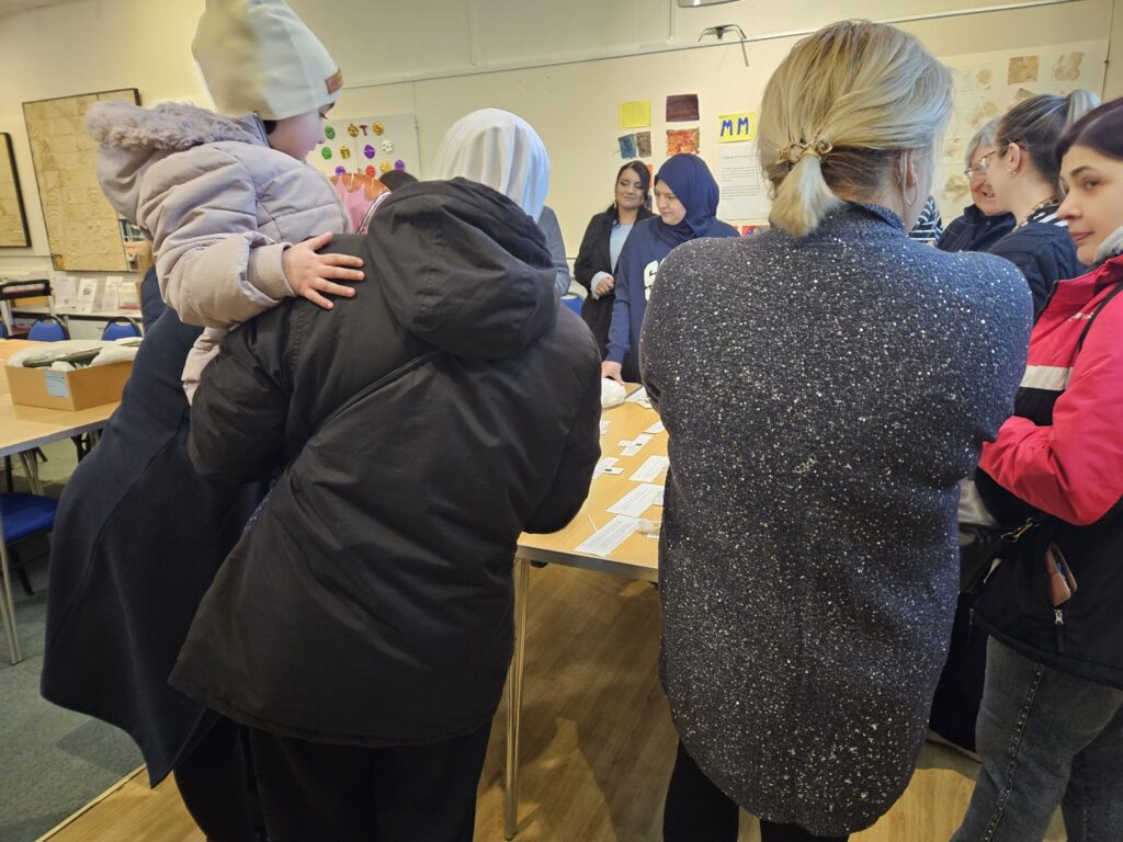A group of women face aways from the viewer to look at objects on a table.