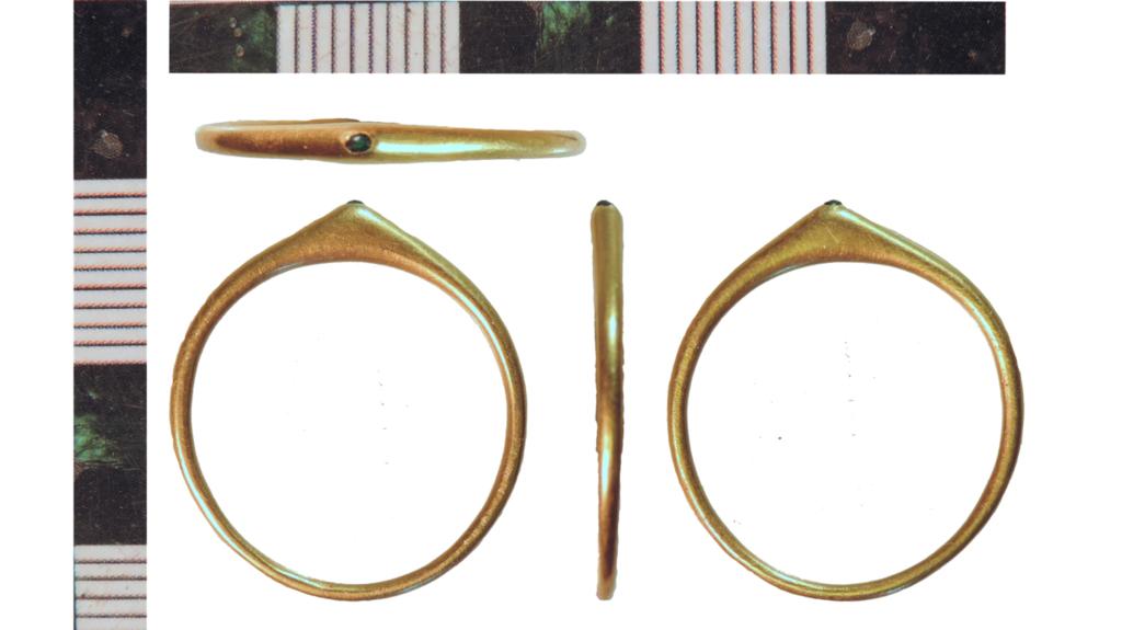 Gold ring with a slim band and a tiny green jewel on the bezel.