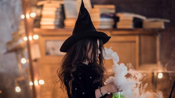 little girl dressed as a witch with a black hat, white smoke is coming from a beaker